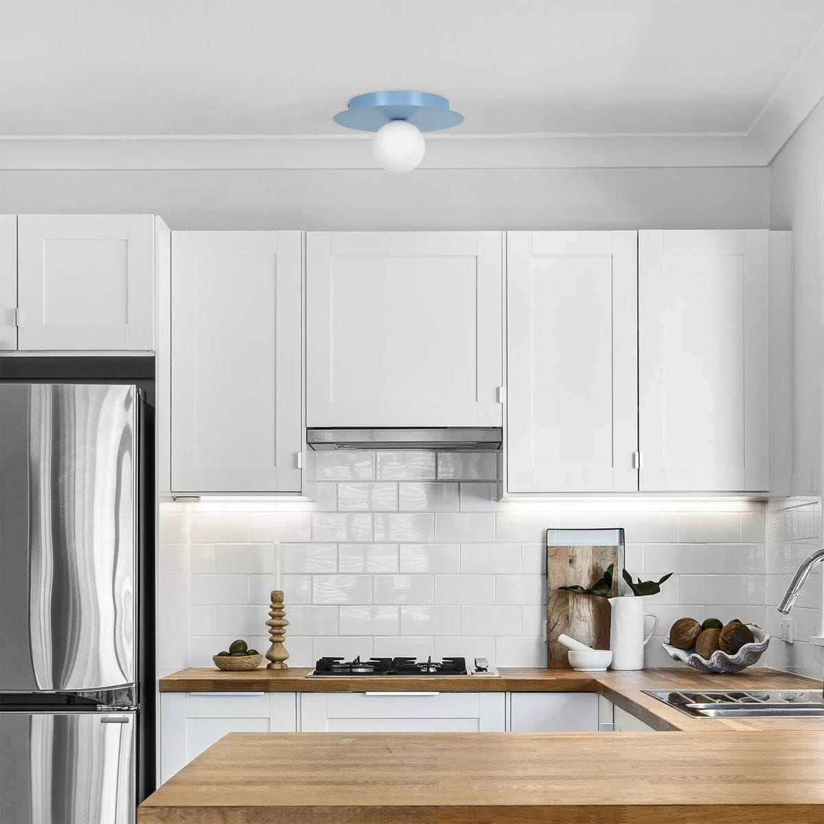 Lampa sufitowa Robin D25 w kolorze niebieskim i białym, z jednym gniazdem G9, zamontowana na suficie w nowoczesnej kuchni. Widoczna okrągła, biała kula światła oraz niebieska podstawa, w otoczeniu białych mebli i drewnianego blatu.