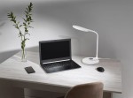 Lampka biurkowa Gaja w kolorze białym, z jedną diodą LED o mocy 9W i regulowanej temperaturze barwowej 3000-5700K. Ustawiona na biurku obok laptopa i telefonu, z wygodnym kształtem oraz podstawą okrągłą. W tle widoczna roślina w szklanym wazonie.
