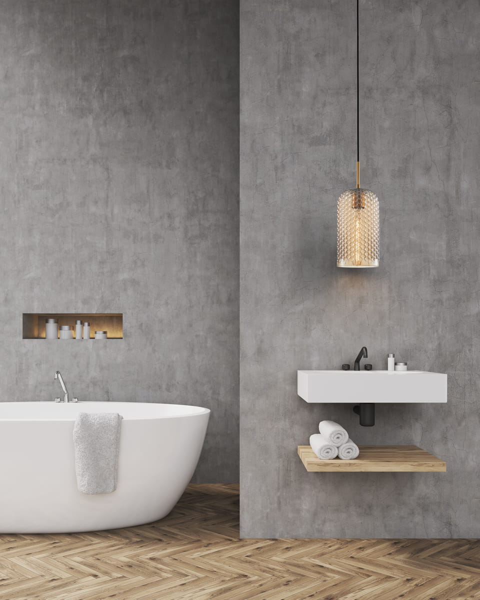 Lampa wisząca Renti 1xE27 w kolorze czarnym z bursztynowym kloszem, umieszczona nad umywalką w nowoczesnej łazience. Klosz ma dekoracyjny wzór, a całość wisi na czarnym przewodzie. Tło stanowi szara ściana i drewniana podłoga.