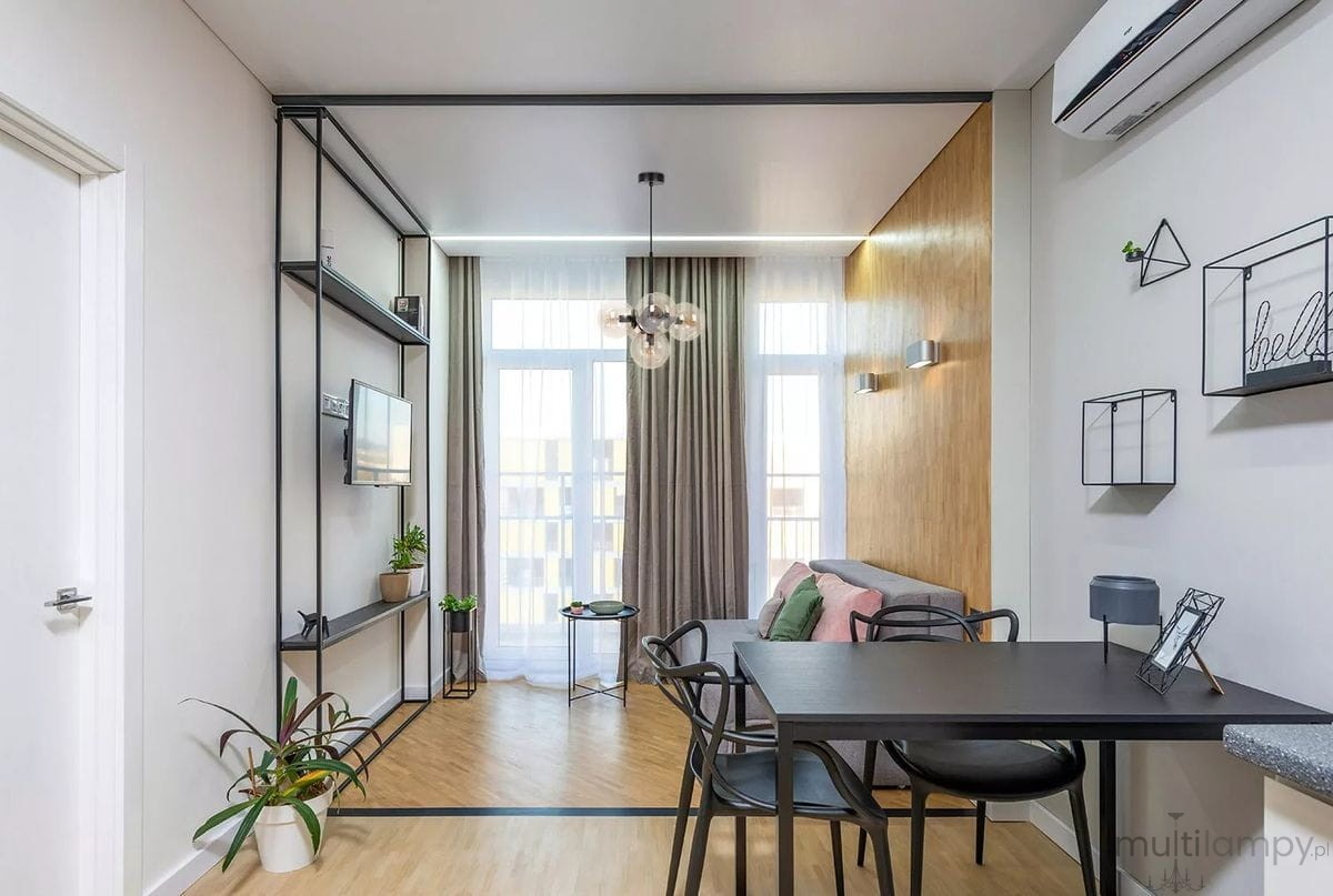 Lampa wisząca Piro w kolorze czarnym z bursztynowymi kloszami, z pięcioma gniazdami E14. Zawieszona w centralnej części pomieszczenia, w nowoczesnym wnętrzu z drewnianymi akcentami i jasnym tłem.