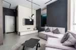 Lampa wisząca Sante D18 w kolorze czarnym i białym, z jedną żarówką G9. Zawieszona na cienkim przewodzie, z okrągłymi, białymi kloszami. Umieszczona w nowoczesnym wnętrzu z szarym narożnikiem, czarnym stolikiem i dużym telewizorem na ścianie.