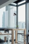 Lampa wisząca Fermi D18 w kolorze czarnym i grafitowym, z jednym gniazdem G9, zawieszona na cienkim przewodzie. Umieszczona w nowoczesnym wnętrzu przy dużych oknach, w pobliżu stołu z drewnianymi nogami i rośliną w doniczce.