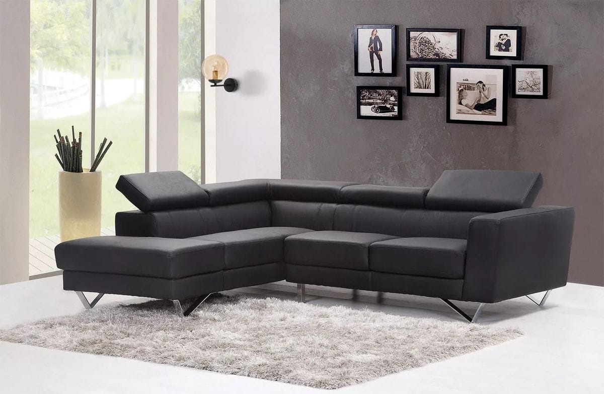 Kinkiet Delta 1xE14 w kolorze czarnym z bursztynowym kloszem. Montowany na ścianie, z widocznym oświetleniem. W tle nowoczesny, czarny narożnik na szarym tle, otoczony jasnym światłem z okien. Wnętrze urządzone w minimalistycznym stylu.