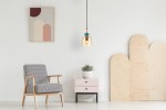 Lampa wisząca Namos 1xE27 w kolorze czarnym i bursztynowym z dekoracyjnym kloszem, zawieszona na cienkim kablu. W tle widać nowoczesne wnętrze z fotelem, stolikiem oraz abstrakcyjnym obrazem.