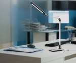 Srebrna lampka biurkowa Rico z jedną diodą LED, mocą 10W i regulowaną temperaturą barwową 3000K-6500K. Ustawiona w pozycji stojącej na biurku, obok myszy komputerowej i dokumentów, z tłem biurowym.