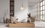 Lampa wisząca Zulo z oprawą w czarnym kolorze, z bursztynowym kloszem w kształcie kropli, zawieszona na czarnym przewodzie. Widoczna w nowoczesnym wnętrzu z beżowymi fotelami i drewnianymi meblami.