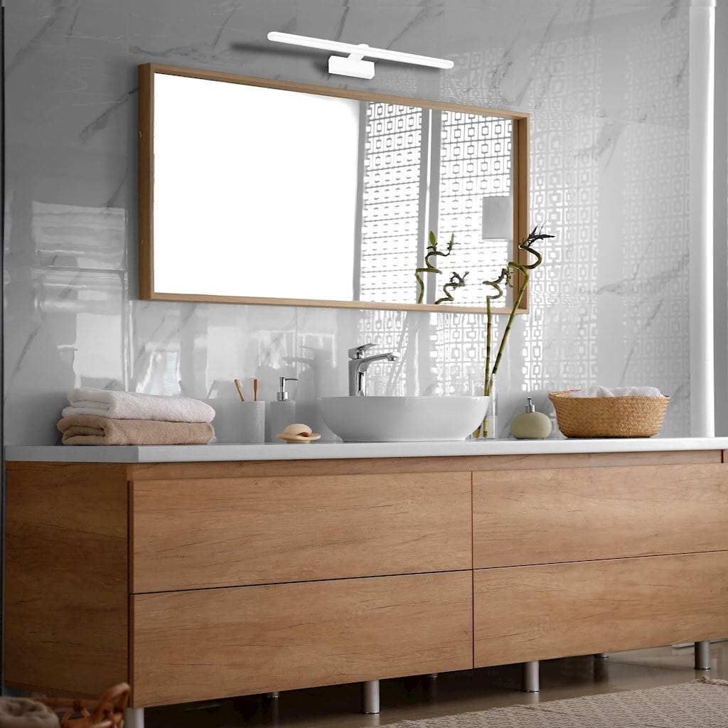 Kinkiet Splash LED IP44 w kolorze białym, zamontowany nad lustrem w łazience. Prosta, minimalistyczna konstrukcja. Widoczne elementy to drewniana rama lustra, umywalka oraz dekoracje, takie jak rośliny i ręczniki na szafce.