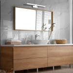Kinkiet Splash LED IP44 w kolorze białym, zamontowany nad lustrem w łazience. Prosta, minimalistyczna konstrukcja. Widoczne elementy to drewniana rama lustra, umywalka oraz dekoracje, takie jak rośliny i ręczniki na szafce.