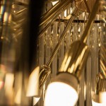 Luxe żyrandol w złotym kolorze, z sześcioma mocowaniami na żarówki E14. Ujęcie z bliska na metalowe elementy i przezroczyste kryształy, które odbijają światło. Widać detale wykończenia i stylowy design.