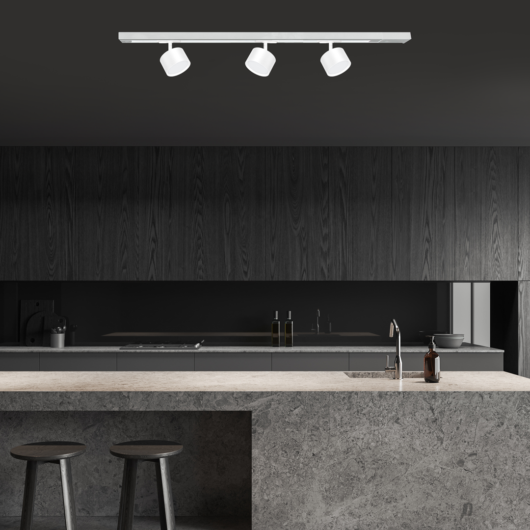 Reflektor Track Cyklop 1xGX53 w kolorze białym, montowany na szynie, z trzema punktami świetlnymi. Ujęcie frontalne w nowoczesnej kuchni z ciemnym drewnem i szarym blatem. Idealny do oświetlenia przestrzeni roboczej.
