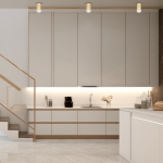 Złota lampa sufitowa Ricky 1xGU10, zamontowana w kuchni, wisi nad białymi szafkami z drewnianymi akcentami. Lampa ma cylindryczny kształt z przezroczystym kloszem, emitującym ciepłe światło. Tło stanowi nowoczesne wnętrze z marmurową podłogą.