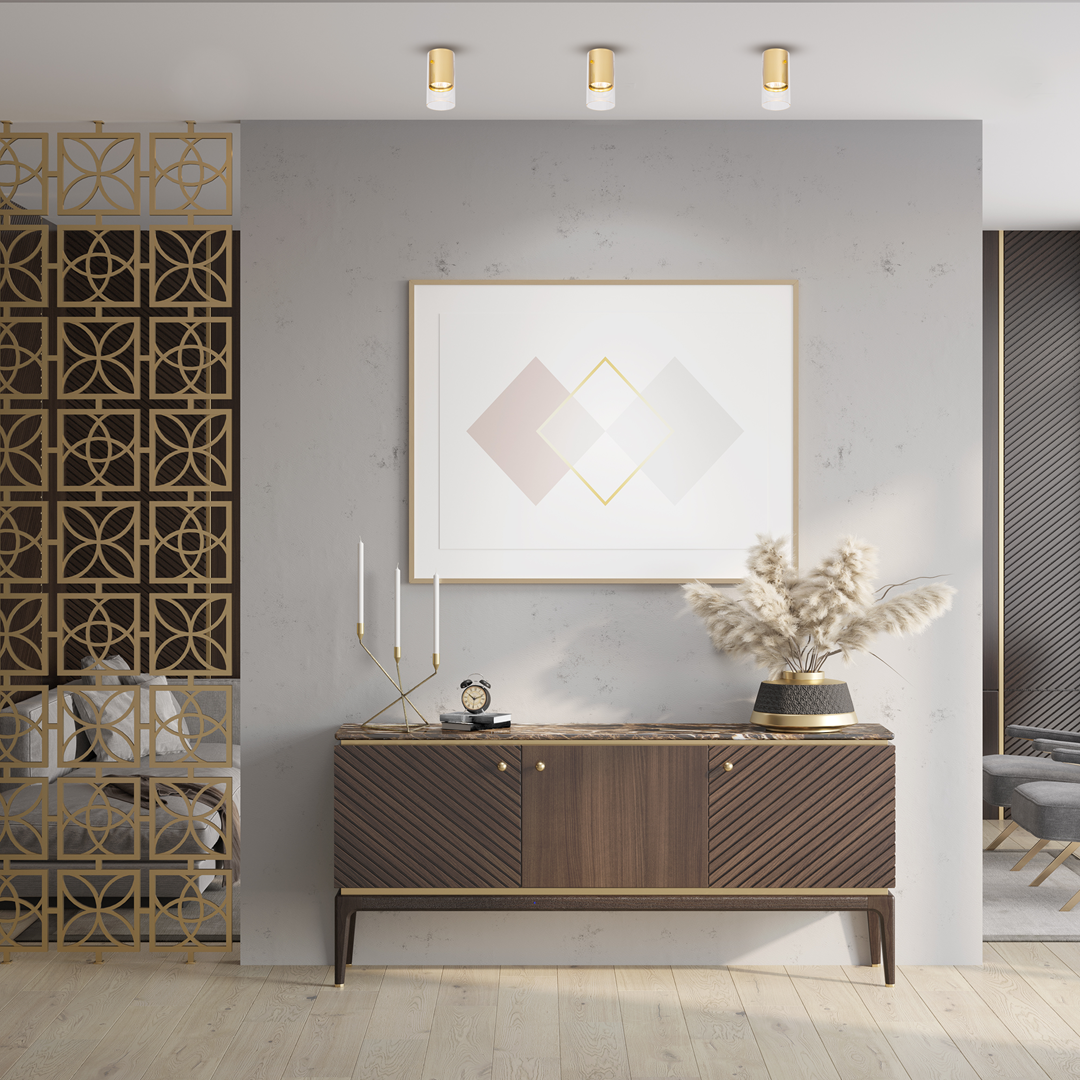 Złota lampa sufitowa Ricky z jednym źródłem światła GU10, zamontowana na gładkim suficie. W tle widoczne eleganckie wnętrze z drewnianą komodą, grafiką na ścianie oraz dekoracjami, w tym świecznikami i roślinami.
