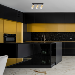 Czarna lampa sufitowa (spot) Ricky z trzema źródłami światła GU10, umieszczona na tle nowoczesnej kuchni z czarnymi i złotymi szafkami. Lampa ma prostokątne, złote klosze, zawieszoną na czarnej ramie.