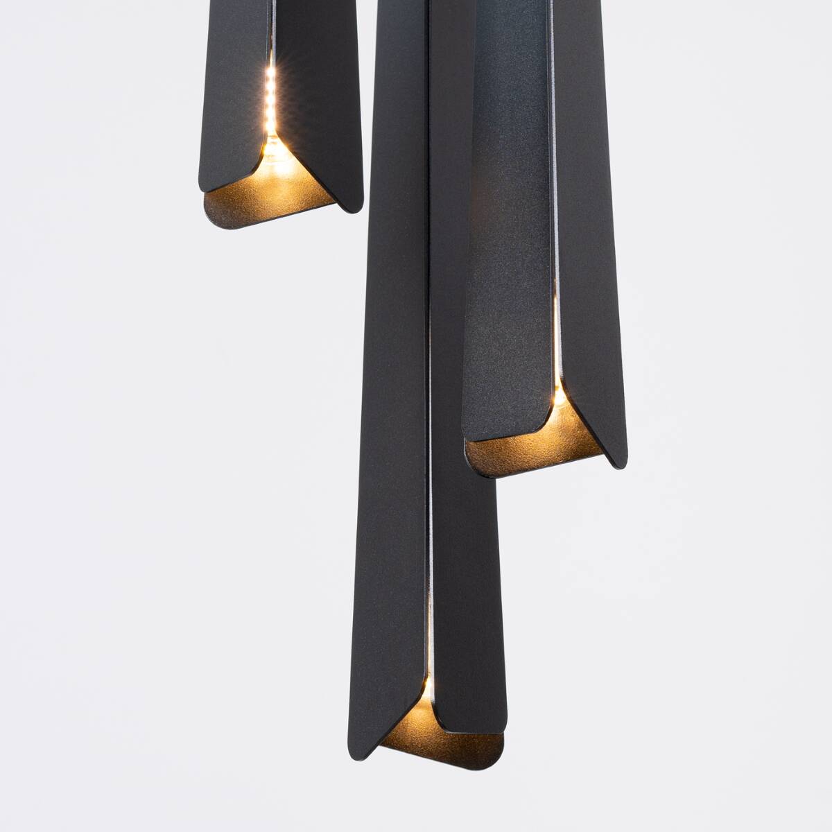 Lampa wisząca Prysm 3P w kolorze czarnym z trzema źródłami światła G9. Kształt w formie wydłużonych, geometrycznych elementów z subtelnym podświetleniem. Produkt zawieszony, w zbliżeniu na detale oświetlenia.
