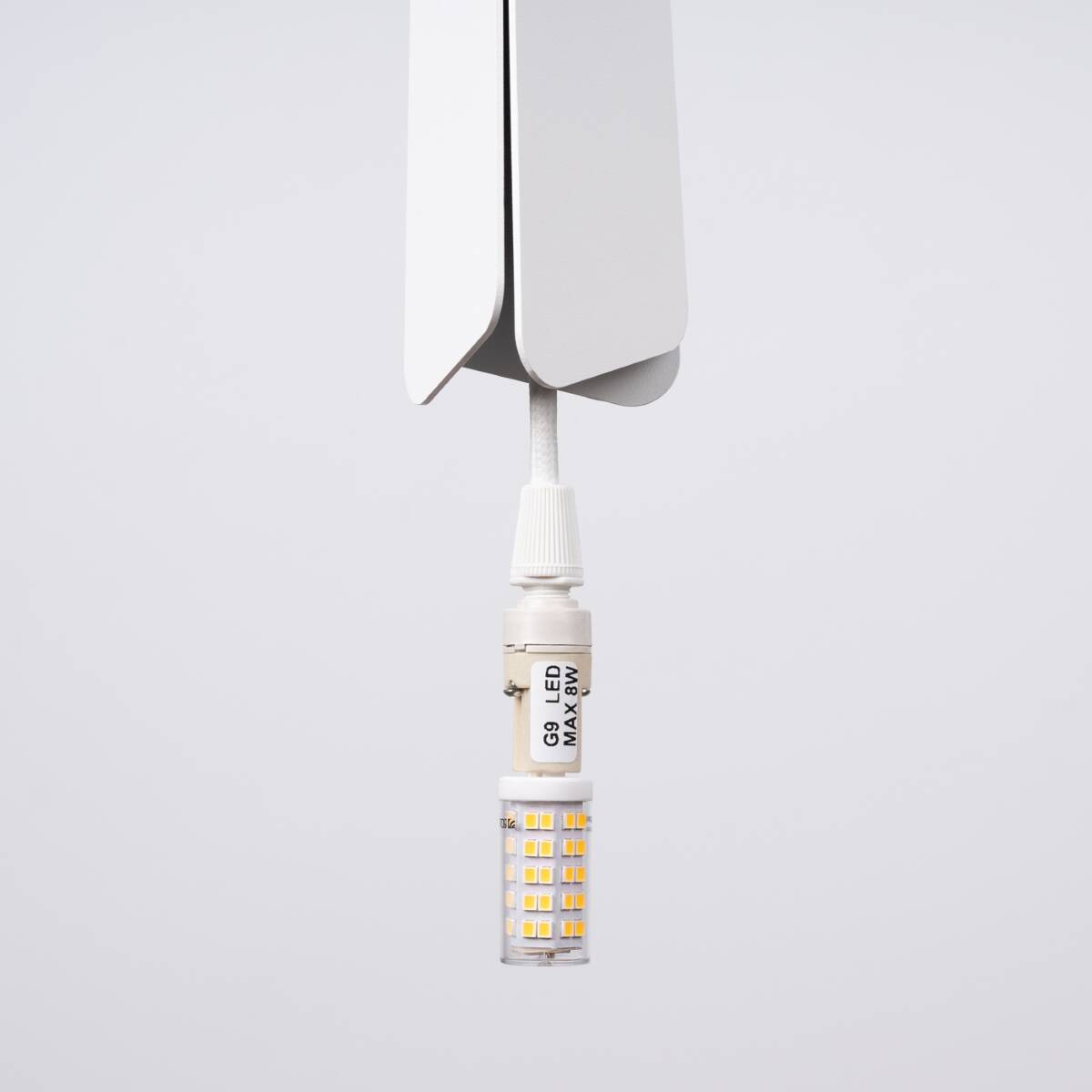 Lampa wisząca Prysm 3P z białym wykończeniem, zawieszona na cienkim kablu. Widoczny element G9 LED o maksymalnej mocy 8W, z przezroczystą obudową i żółtymi diodami. Prosty, nowoczesny design, idealny do różnorodnych wnętrz.