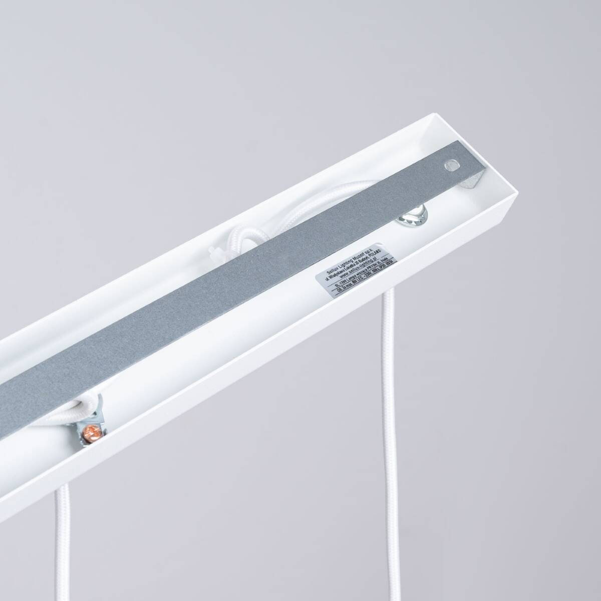 Lampa wisząca Prysm z białym wykończeniem, z miejscem na trzy żarówki G9. Widoczna metalowa podstawa oraz białe przewody. Kąt ujęcia z góry, ukazujący detale instalacyjne. Tło szare, proste, podkreślające produkt.