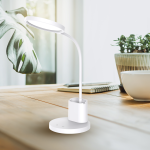 Lampa biurkowa Scuola w kolorze białym z elastycznym ramieniem. Okrągła podstawa z przyciskiem dotykowym, zintegrowane źródło światła LED o mocy 8W. W tle widoczna roślina oraz notatnik na drewnianym stole.