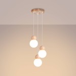 Lampa wisząca Pekka 3P z trzema okrągłymi kloszami, wykonana z drewna. Klosze w kolorze białym zawieszone na białych przewodach, z drewnianymi elementami na górze. Produkt zamontowany na okrągłej podstawie. Tło w jednolitym beżowym odcieniu.