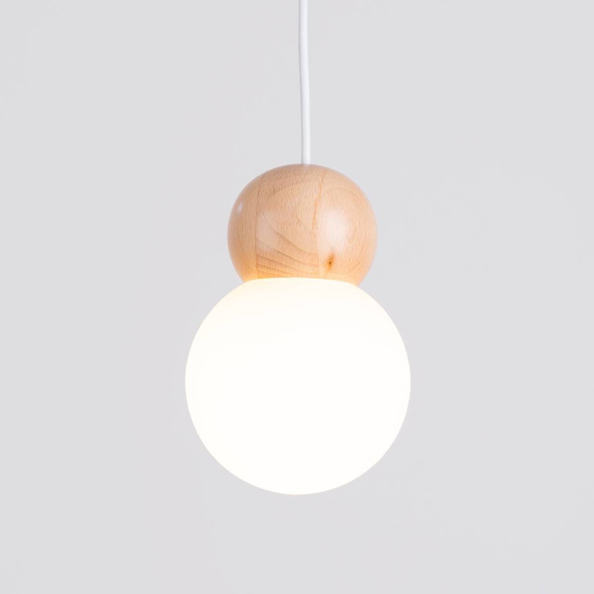Lampa wisząca Pekka 3P z drewnianym elementem w kolorze naturalnym i białą, okrągłą szklaną kloszem. Produkt zawieszony na białym przewodzie, w zbliżeniu na detale konstrukcji. Idealna do nowoczesnych wnętrz.