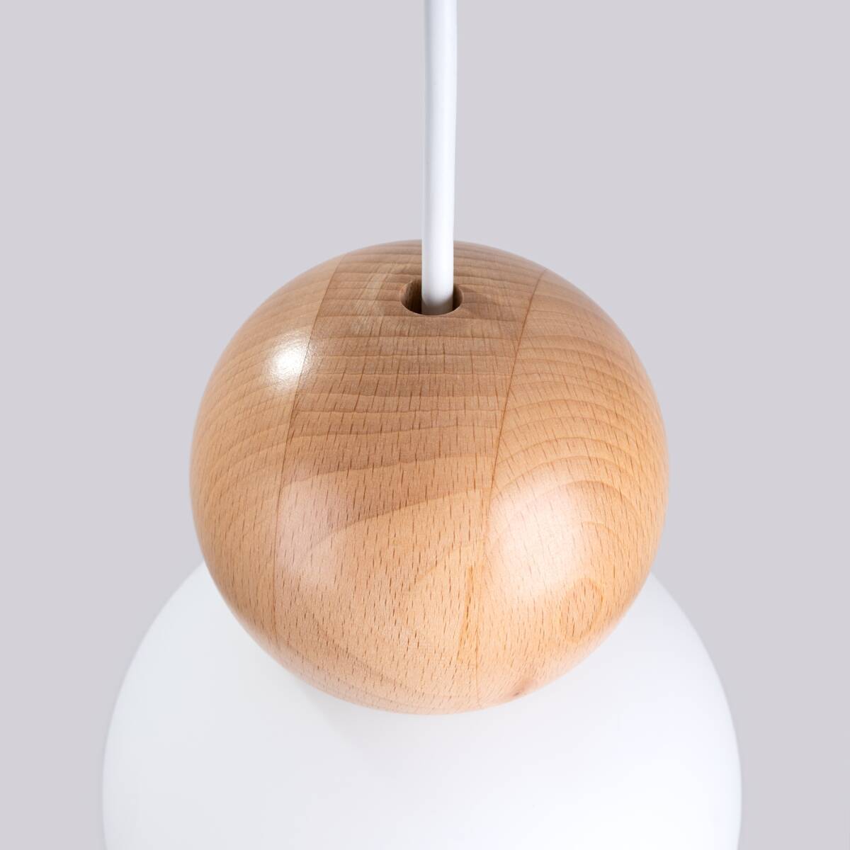 Lampa wisząca Pekka 3P z drewnianym elementem w kształcie kuli, zawieszona na białym przewodzie. Widoczna tekstura drewna, gładka powierzchnia. Tło szare, podkreślające detale produktu. Przeznaczenie do lamp G9.