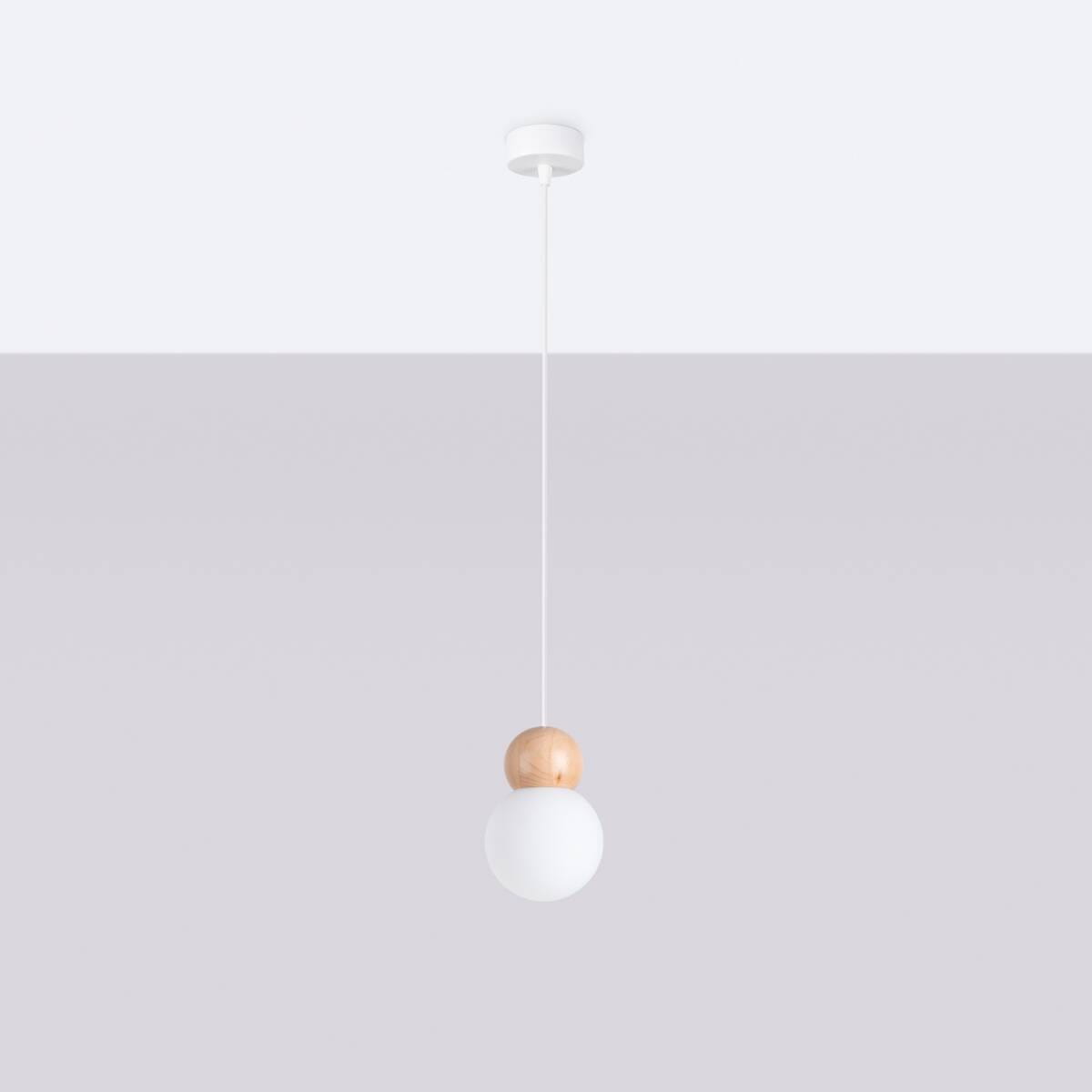 Lampa wisząca Pekka z pojedynczym źródłem światła G9, zawieszona na cienkim białym przewodzie. Posiada okrągły klosz z matowego szkła oraz drewnianą, jasną kulę u góry. Tło w odcieniach szarości, minimalistyczny design.