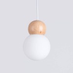 Lampa wisząca Pekka z drewna, składająca się z białej, matowej kulistej klosza oraz drewnianej, okrągłej podstawy. Zawieszona na białym przewodzie, w układzie frontalnym na jednolitym tle. Idealna do nowoczesnych wnętrz.