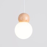 Lampa wisząca Pekka z drewnianym elementem, zawieszona na białym przewodzie. Okrągła, mleczna kula świetlna z górnym, naturalnym drewnianym kulistym akcentem. Prosty, nowoczesny design na jasnym tle.