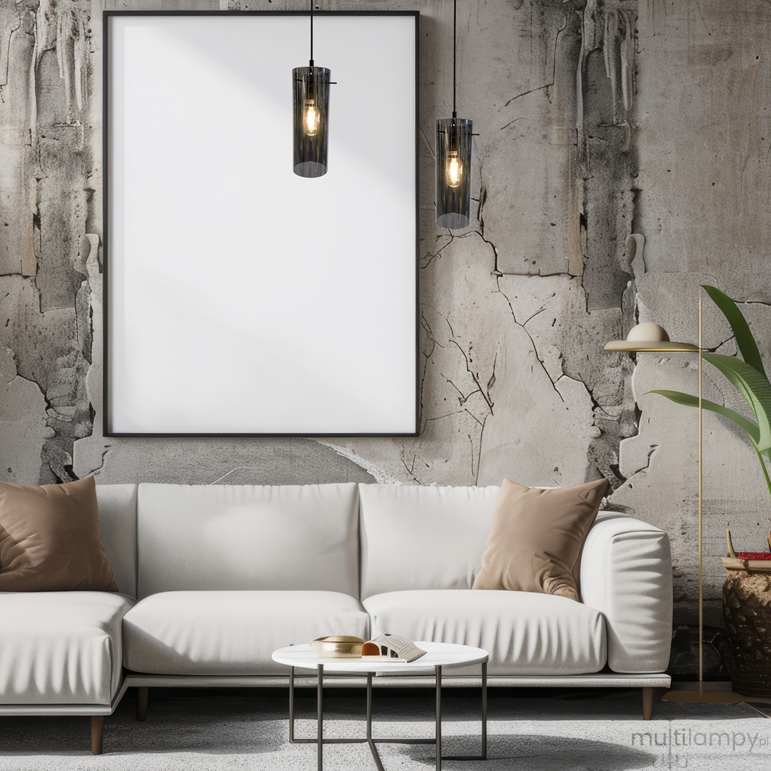 Lampa wisząca Padova 1xE27 w kolorze czarnym, o cylindrycznym kształcie z przezroczystym kloszem, zawieszona nad białą sofą w nowoczesnym wnętrzu z szarymi ścianami i minimalistycznym wystrojem.