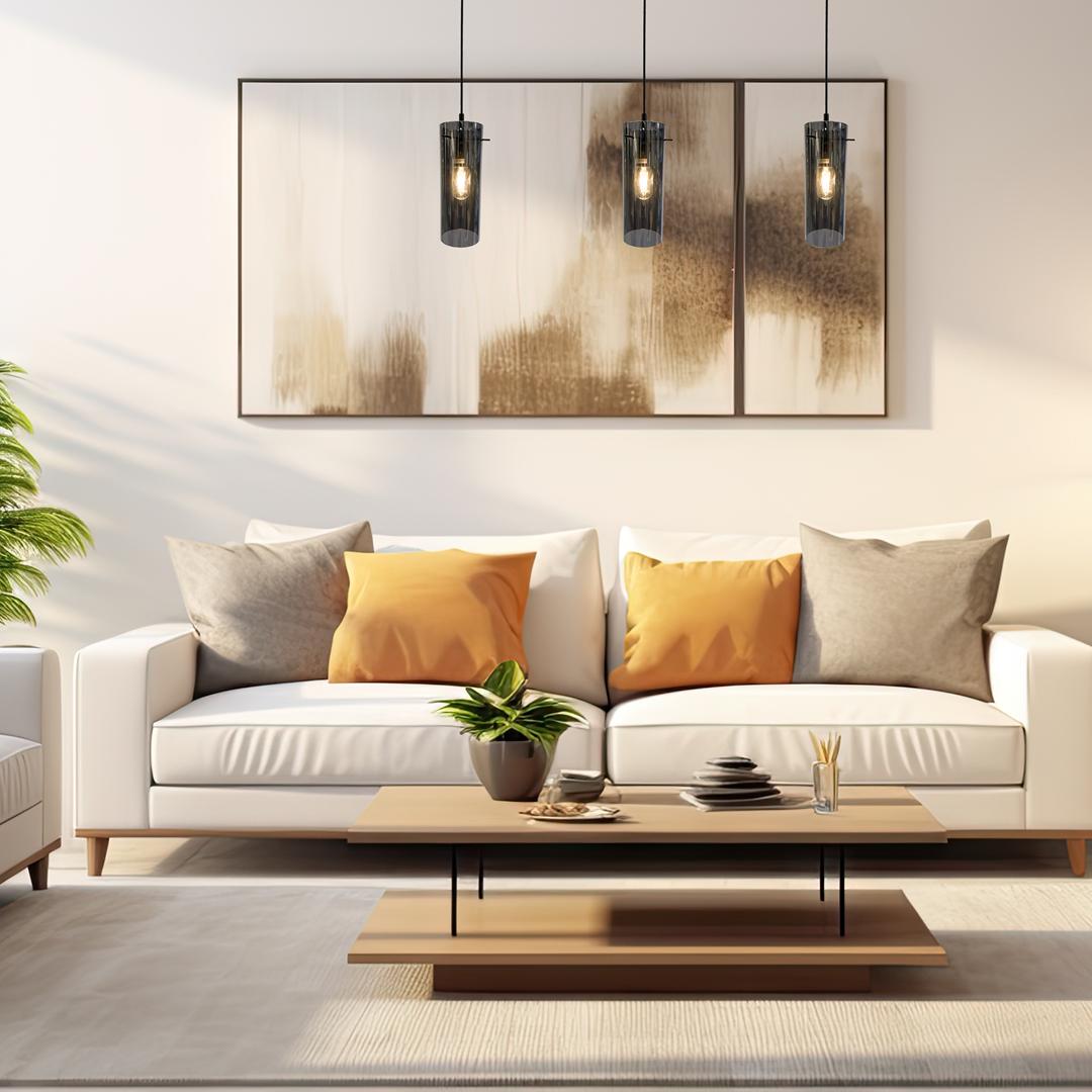 Lampa wisząca Padova 3xE27 w kolorze czarnym, o cylindrycznym kształcie, zawieszona na cienkich linkach. W tle widoczny jasny salon z białą sofą, poduszkami w odcieniach szarości i pomarańczy oraz drewnianym stolikiem.