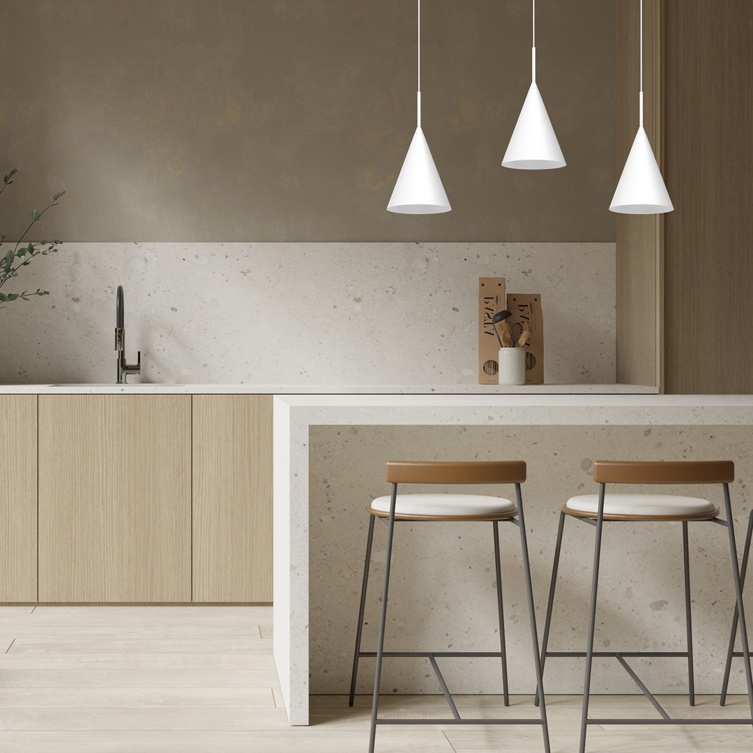 Lampa wisząca Capital D17 w kolorze białym, z kształtem stożkowatym, zawieszona nad białym blatem w kuchni. W tle drewniane szafki i minimalistyczne dekoracje. W zestawie trzy lampy, zawieszone na cienkich kabelkach, tworzą harmonijną aranżację.