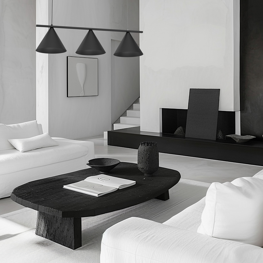 Czarna lampa wisząca Capital z trzema kloszami w kształcie stożków, zawieszona nad okrągłym, czarnym stołem. Lampa ma minimalistyczny design, a w tle znajduje się nowoczesny salon w odcieniach bieli i czerni.