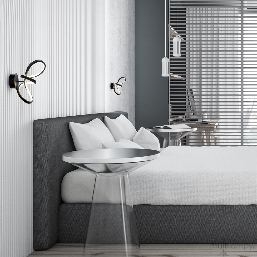 Kinkiet Tesoro 1xLED/15W w kolorze czarnym, zamontowany na ścianie nad łóżkiem. Posiada nowoczesny, minimalistyczny design z delikatnymi, podświetlonymi detalami. W tle widoczna jasna pościel i szklany stolik nocny w nowoczesnej sypialni.