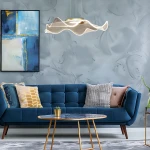 Lampa wisząca Largo z jedną żarówką LED 16W w kolorze złotym, o falistym kształcie, zawieszona nad niebieską sofą. Tło w odcieniach szaro-niebieskich z obrazem na ścianie oraz okrągłym stołem kawowym.