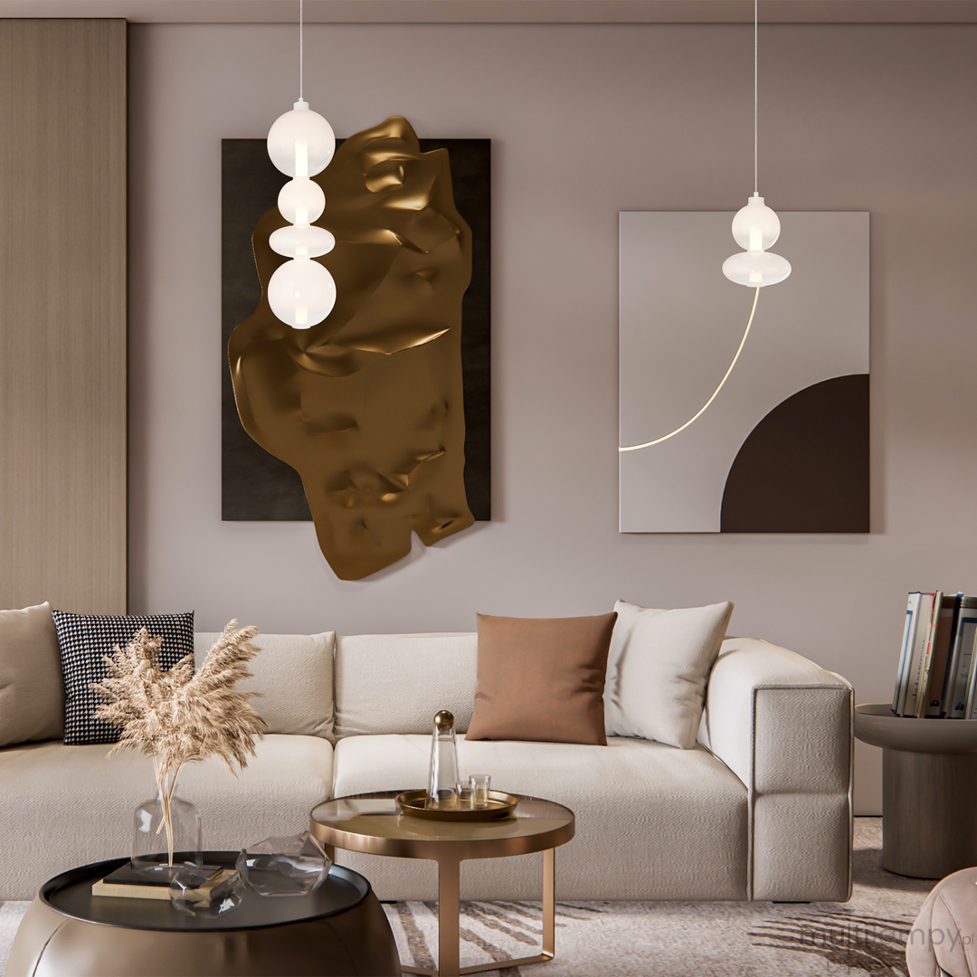 Lampa wisząca Daphne w kolorze białym, z jedną żarówką LED o mocy 36W. Okrągłe klosze w formie kul, zawieszone na cienkim przewodzie, w nowoczesnym wnętrzu z beżową sofą i złotą dekoracją na ścianie.