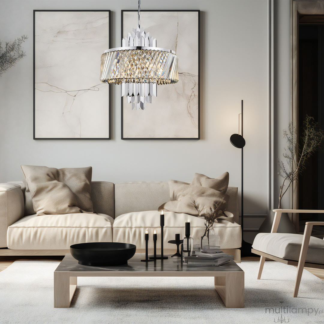 Lampa wisząca Margot w kolorze chromu, z dziewięcioma miejscami na żarówki E14. Posiada ozdobne detale w formie kryształów, zawieszona w nowoczesnym wnętrzu z beżową sofą i minimalistycznymi dekoracjami.