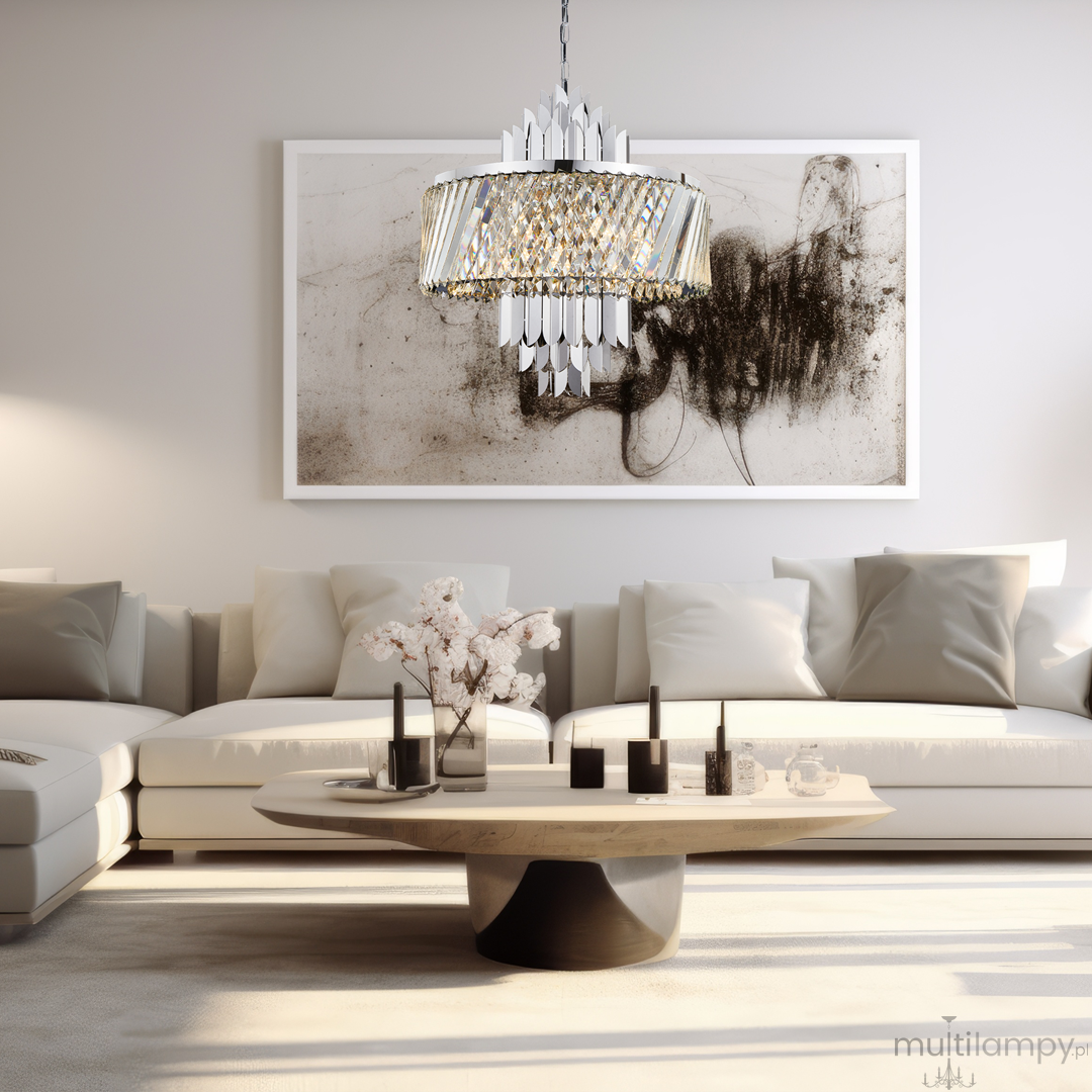 Lampa wisząca Margot w kolorze chromu, z 9 miejscami na żarówki E14. Ozdobiona kryształowymi elementami, ma okrągły klosz z dekoracyjnymi detaliami. Zawieszona w nowoczesnym wnętrzu, nad niskim stołem kawowym.