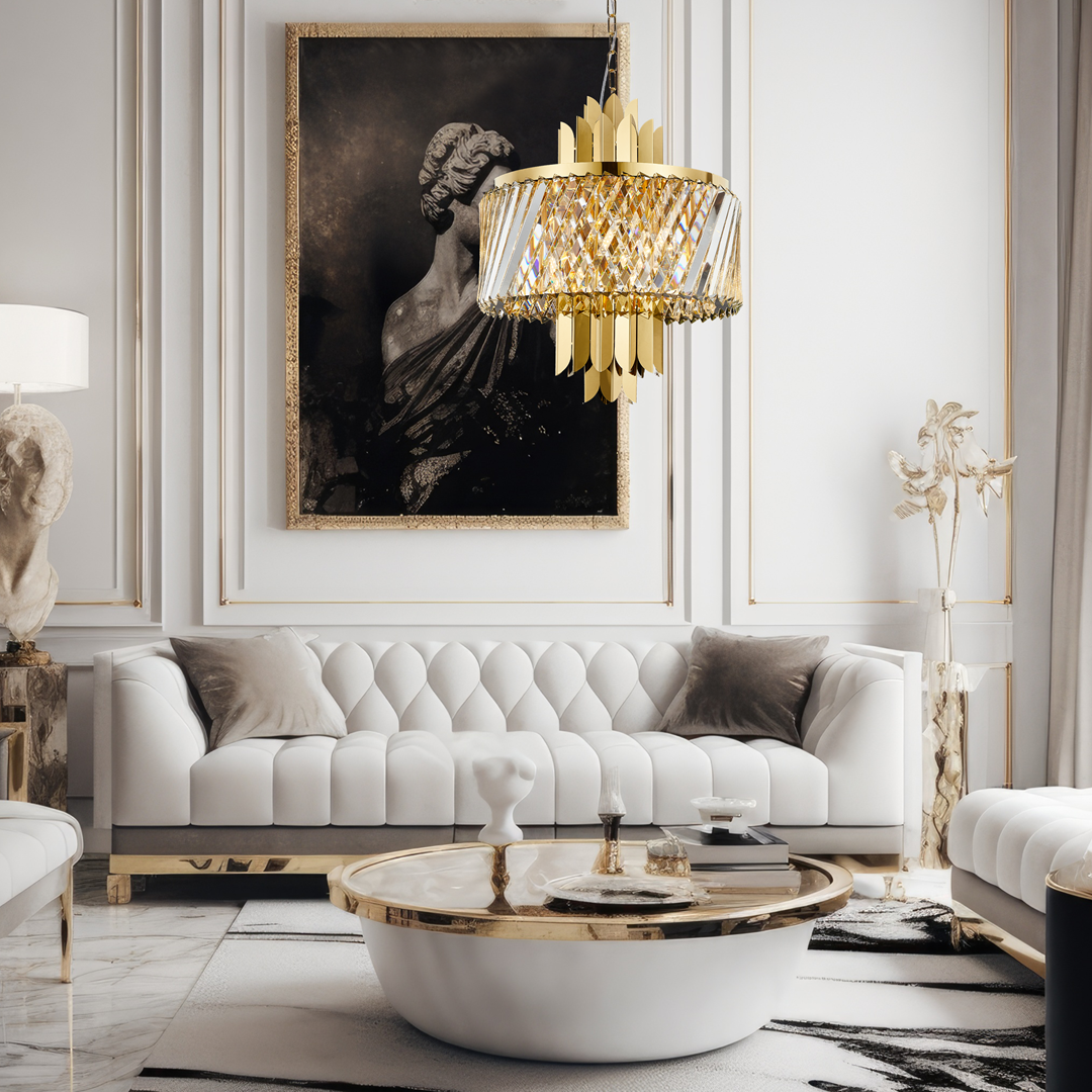 Lampa wisząca Margot w kolorze złotym, z sześcioma oprawami E14, z kryształowym kloszem i dekoracyjnymi elementami. Zawieszona w eleganckim wnętrzu z białą sofą i okrągłym stolikiem kawowym.