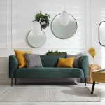 Lampa wisząca Braga 1xE27 w kolorze chromu i białym, z okrągłym kształtem. Zawieszona nad zieloną sofą z poduszkami w odcieniach żółtego i czarno-białym wzorem. Tło jasne, z lustrami i roślinami, tworzy nowoczesną aranżację wnętrza.