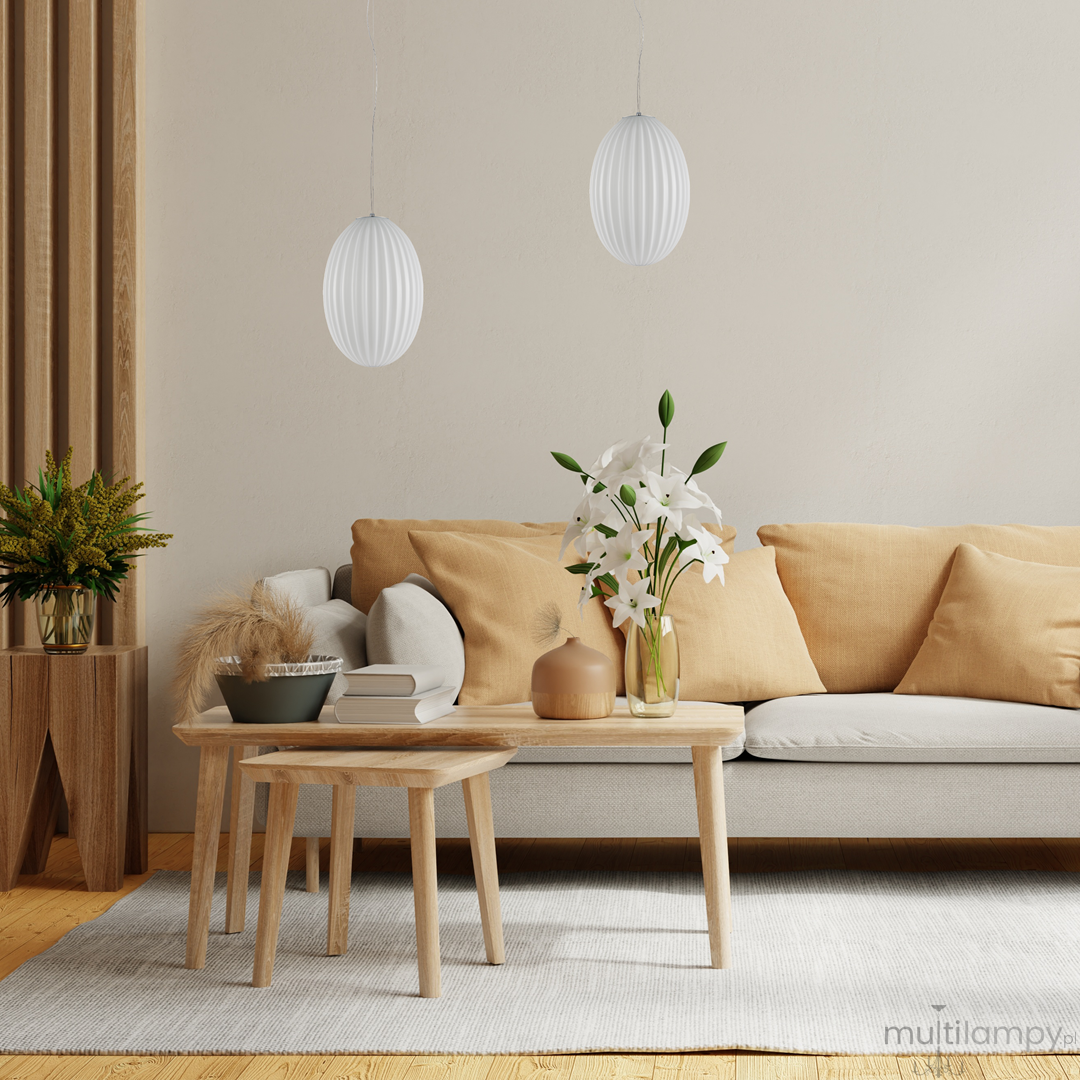 Lampa wisząca Braga 1xE27 w kolorze chromu i białym, o owalnym kształcie z żłobieniami, zawieszona na cienkim kablu. W tle nowoczesny salon z jasną sofą, drewnianymi stolikami i wazonem z białymi kwiatami.