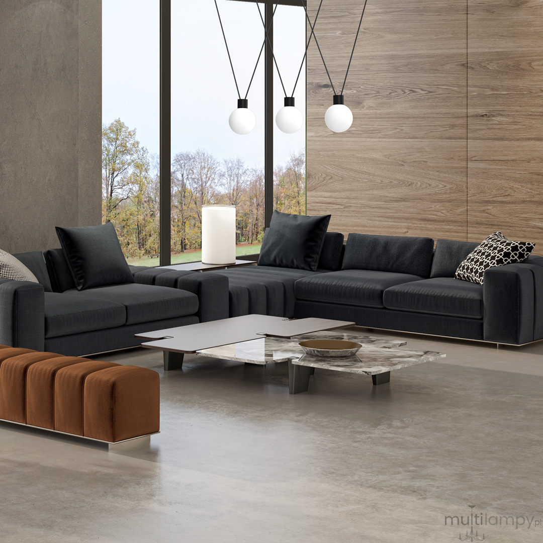 Lampa wisząca Capri 3xG9 w czarnym kolorze z białymi kloszami, zawieszona nad nowoczesnym, ciemnoszarym zestawem wypoczynkowym w jasnym wnętrzu. Widoczne okno z widokiem na zewnątrz oraz stół kawowy z marmurowym blatem.