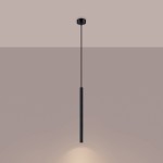 Lampa wisząca Arche w kolorze czarnym, z pojedynczym źródłem światła G9. Ma prostą, cylindryczną formę z teksturowaną powierzchnią. Zawieszona na cienkim, czarnym przewodzie, emitując światło w dół. Tło w odcieniu jasnego beżu.