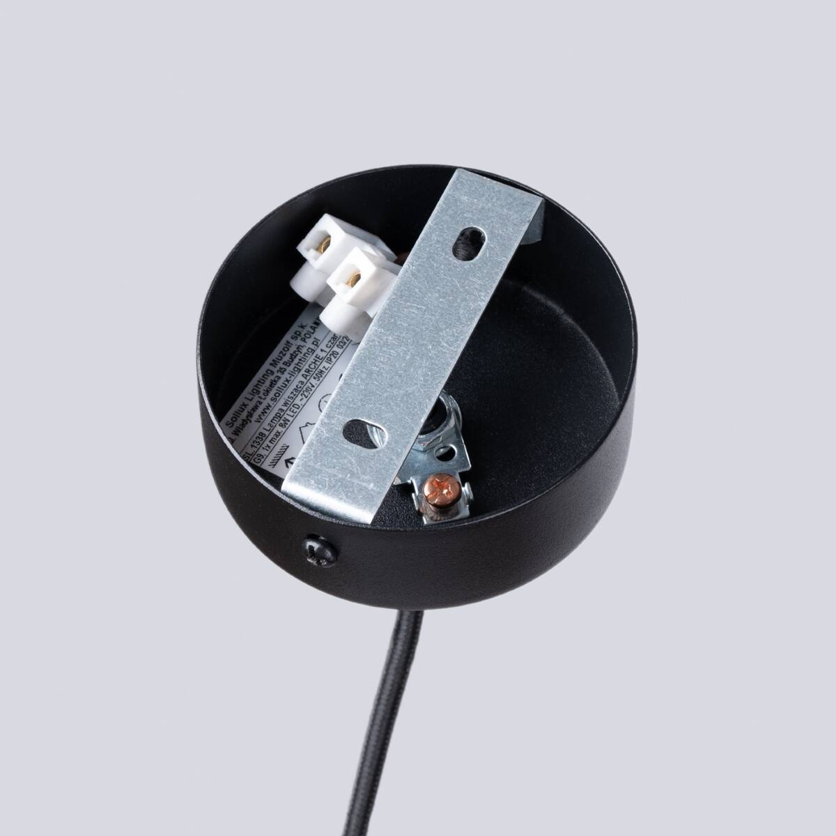 Czarna lampa wisząca Arche z miejscem na jedną żarówkę G9. Widok z góry na okrągłą podstawę, metalowy uchwyt montażowy oraz połączenia elektryczne. Tło szare, minimalistyczne.