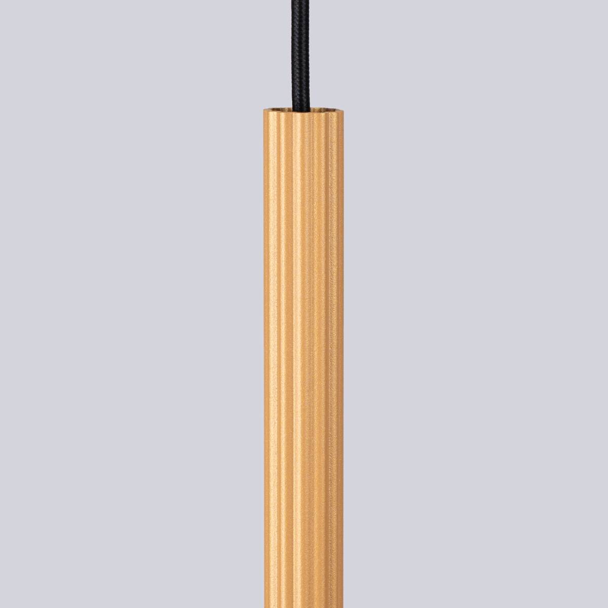 Lampa wisząca Arche w kolorze złotym, wykonana z aluminium, ma prostą, cylindryczną formę z delikatnym rowkowaniem. Zawieszona na czarnym przewodzie, idealna do nowoczesnych wnętrz.
