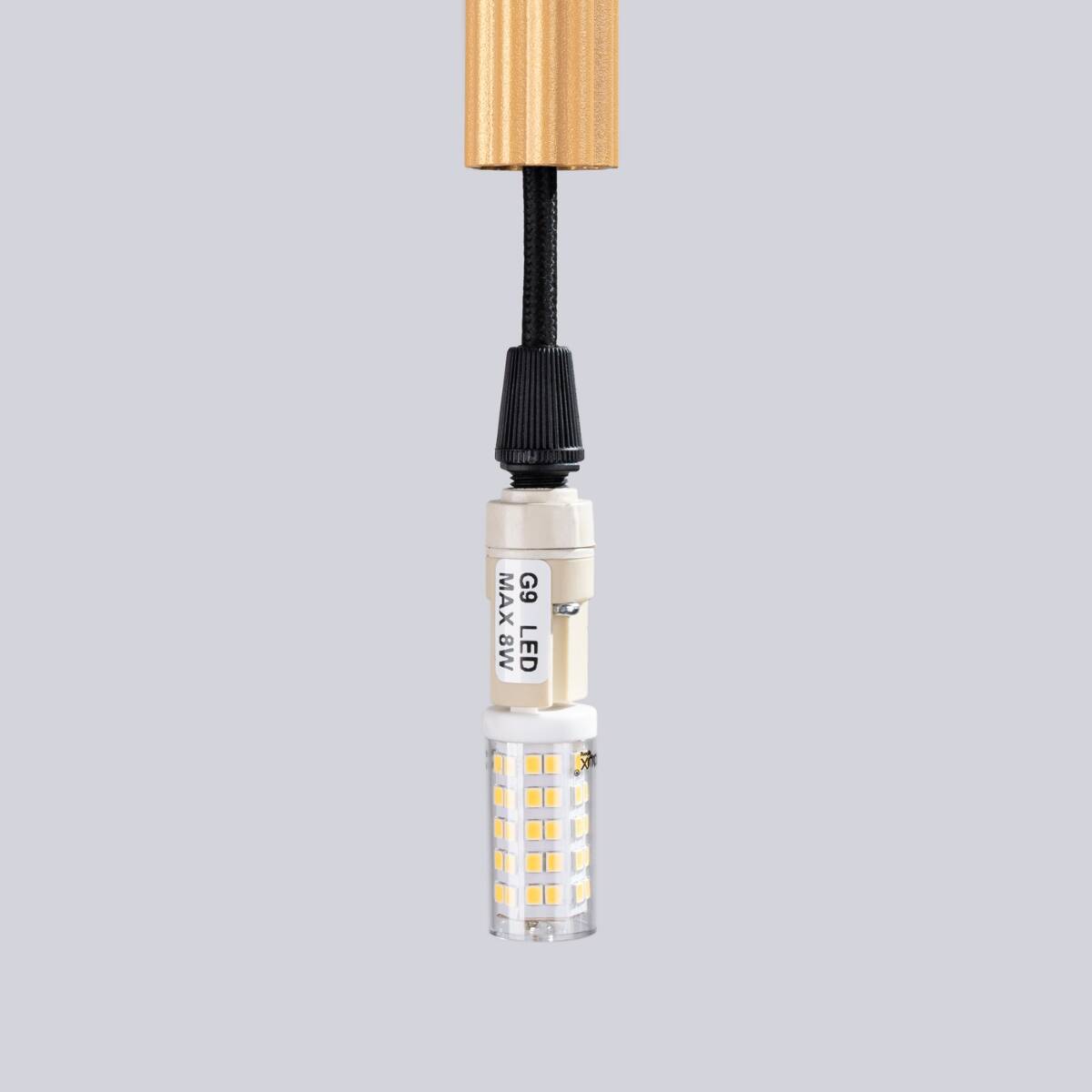 Lampa wisząca Arche 1xG9 w kolorze złotym. Widoczny detal gniazda G9 z diodami LED, umieszczony na czarnym przewodzie. Górna część lampy jest złota, a dolna część przezroczysta z widocznymi diodami. Tło szare.