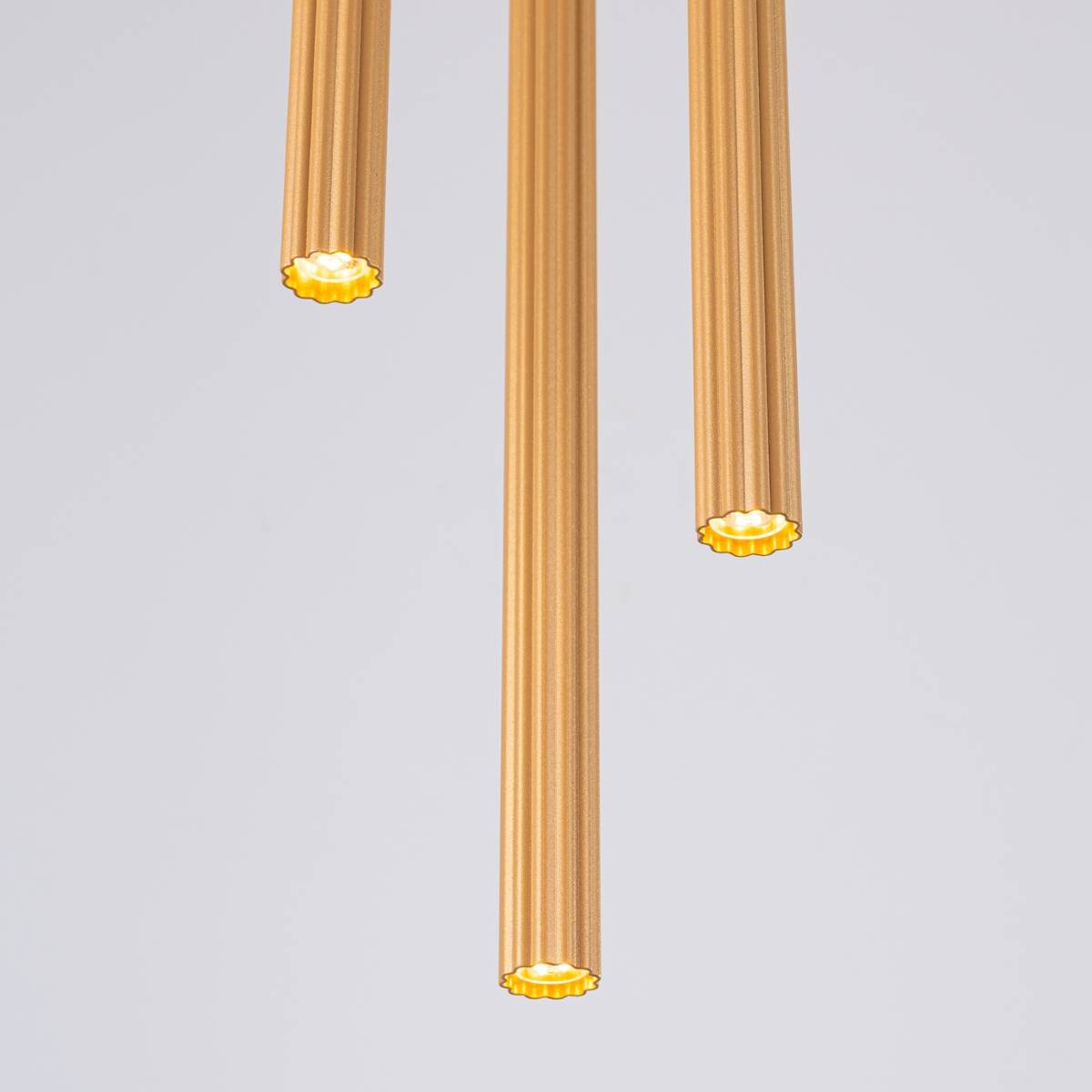 Lampa wisząca Arche z trzema tubami w kolorze złotym, wykonana z metalowego materiału o teksturowanej powierzchni. Ujęcie z góry, ukazujące detale końcówek z żarówkami G9. Tło jasne, podkreślające elegancję lampy.