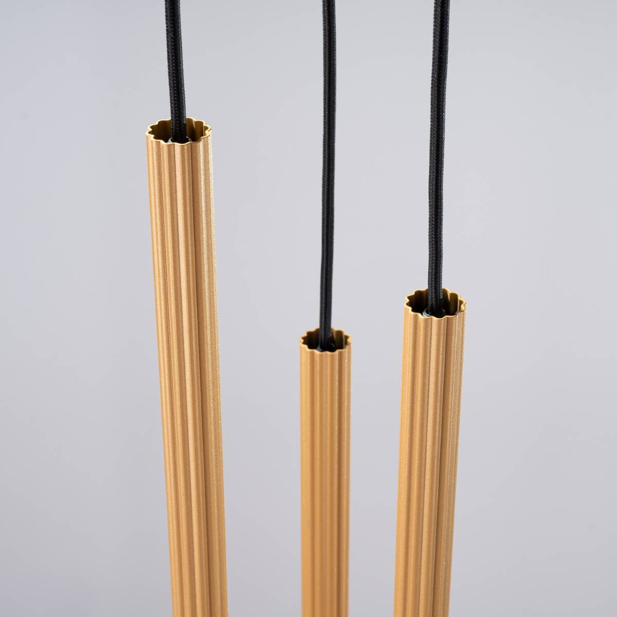 Lampa wisząca Arche 3xG9 w kolorze złotym, składająca się z trzech cylindrycznych elementów o żłobionej fakturze. Elementy zawieszone na czarnych przewodach, prezentowane na szarym tle.