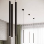 Lampa wisząca Arche, czarna, z trzema cylindrycznymi kloszami, zawieszona na cienkich linkach. Widoczna w nowoczesnym wnętrzu z jasnym tłem oraz zasłonami. Klosze mają teksturowaną powierzchnię, strefy oświetleniowe na dole.