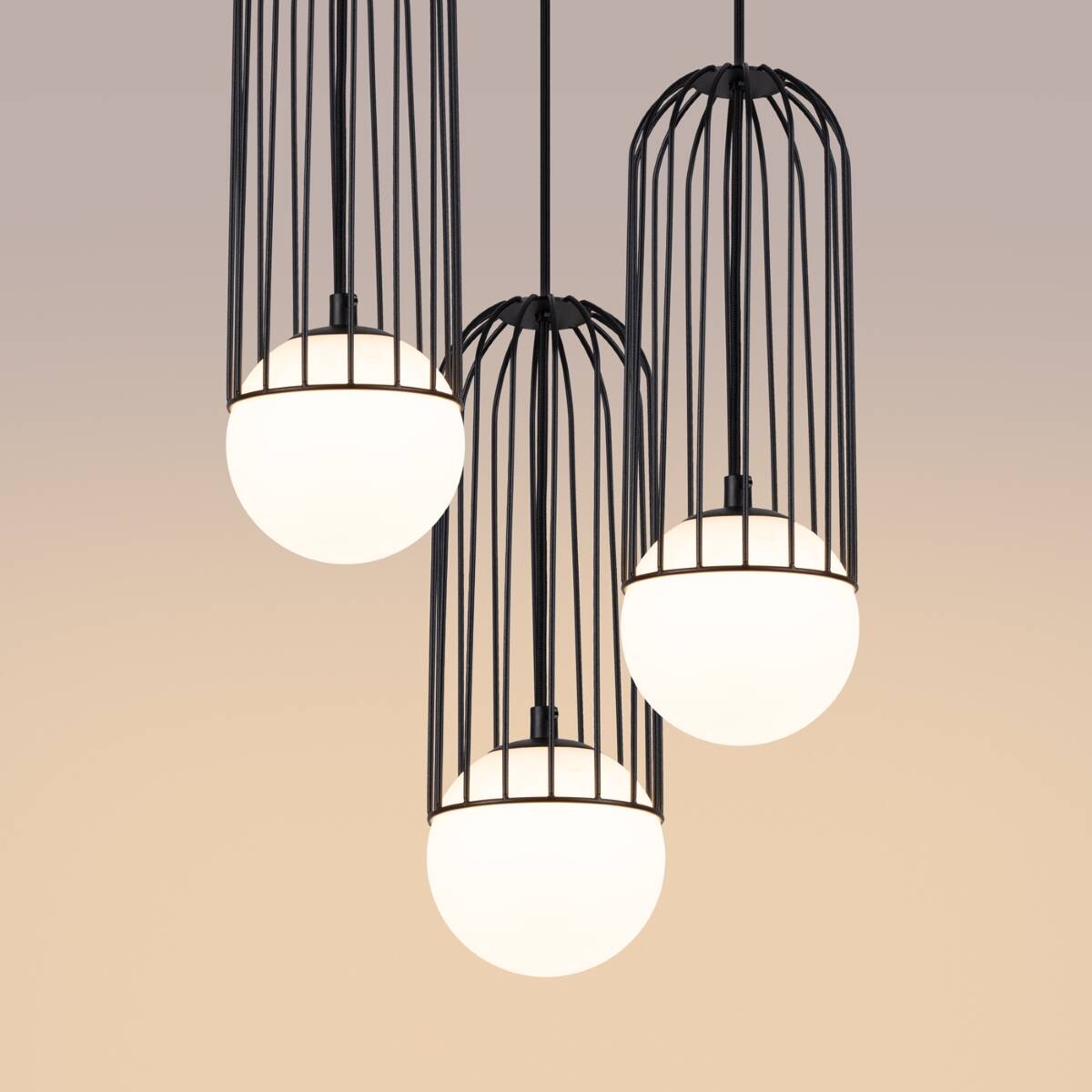 Lampa wisząca Brina 3P z trzema kloszami w kształcie kul, osłoniętymi czarną metalową siatką. Wisi na cienkich kablach, z białymi, szklanymi kulami emitującymi światło. Tło w odcieniach beżu, podkreślające elegancję lampy.