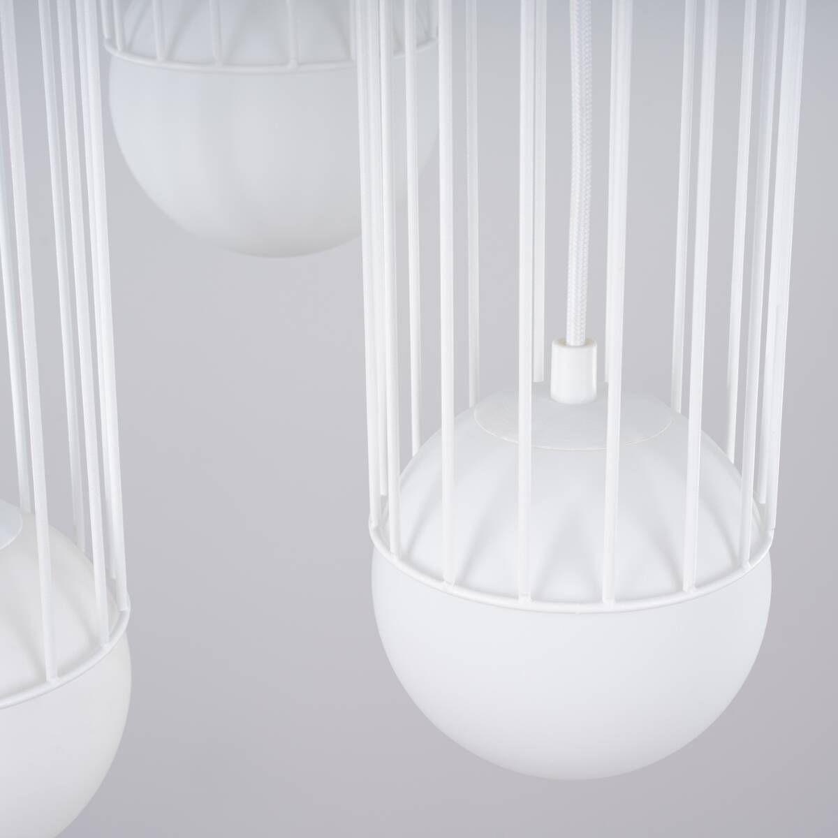 Lampa wisząca Brina 3P z trzema źródłami światła G9, w białej kolorystyce, z okrągłymi kloszami osadzonymi w metalowej, białej siatce. Widok zbliżony, ukazujący detale kloszy i zawieszenia. Tło jasne, jednolite.