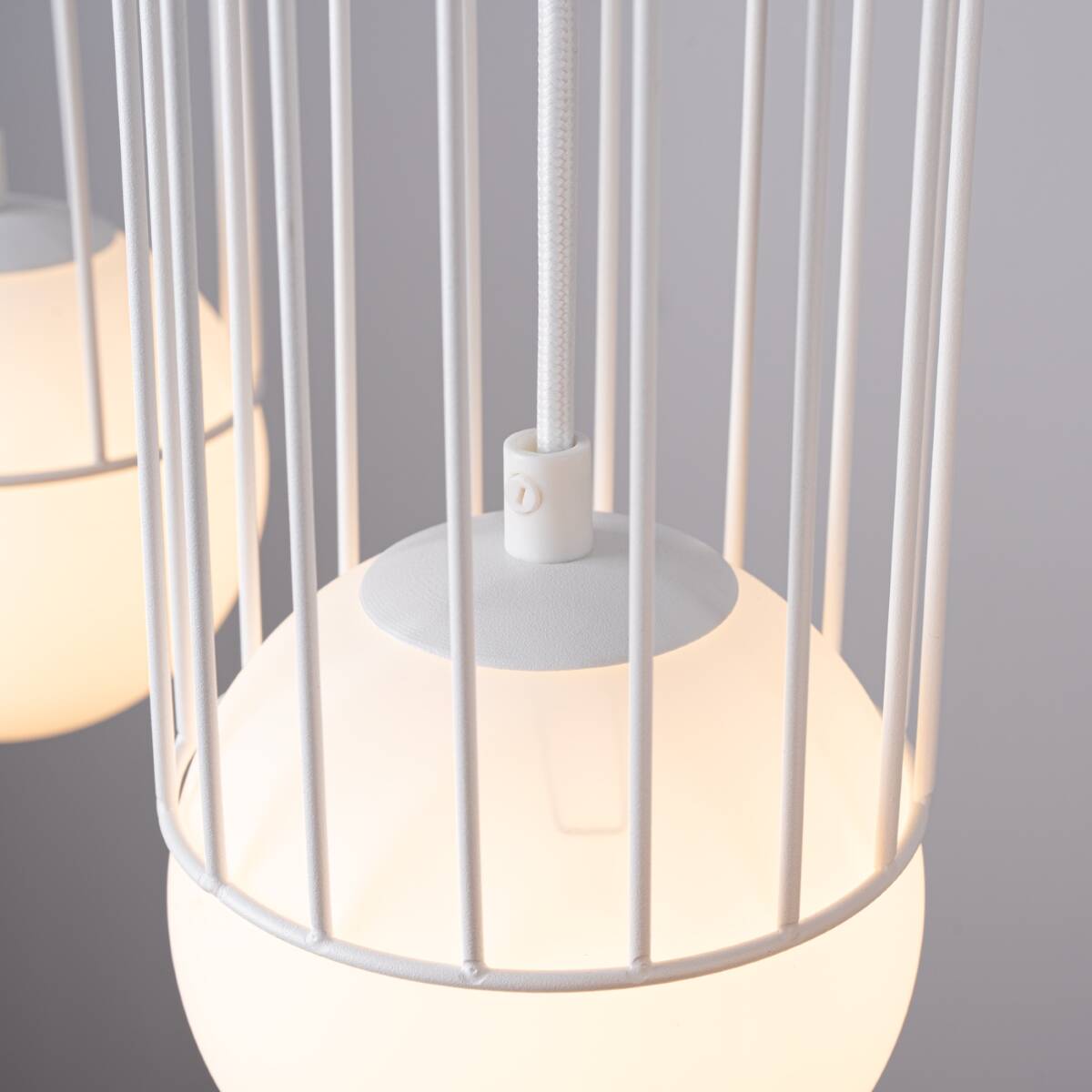 Lampa wisząca Brina 3xG9 w kolorze białym, z okrągłym, mlecznym kloszem osłoniętym metalową, białą siatką. Widać zawieszenie na białym przewodzie. Ujęcie zbliżeniowe na detal lampy, podkreślające subtelną konstrukcję i nowoczesny design.